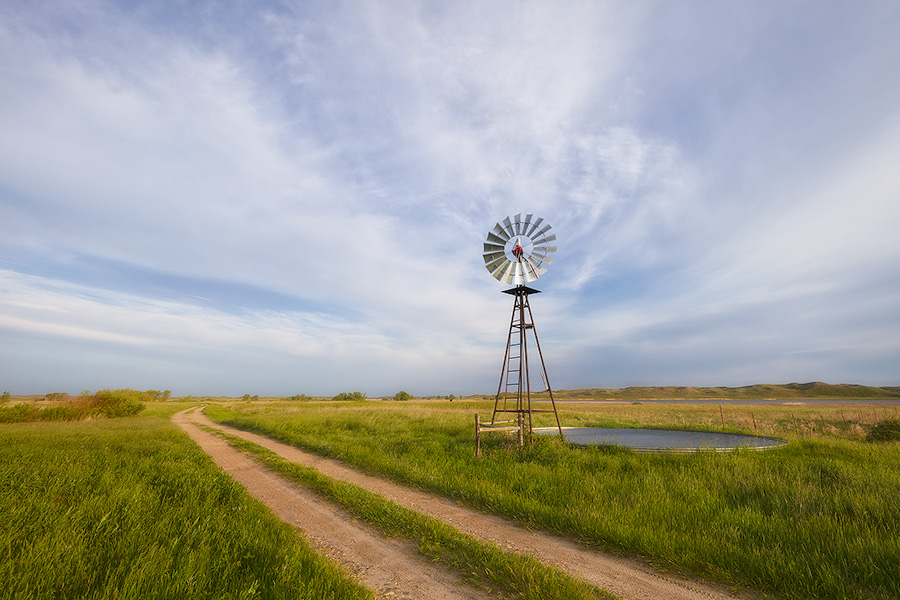 In an area of the Sandhills of Nebraska, far from civilization a two-track road meanders by a windmill and a lake nestled in the hills. - Nebraska Photography