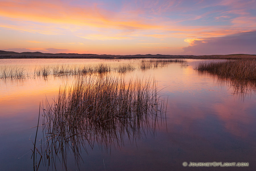 On a cool and quiet spring evening, the sun illuminates the clouds hanging over Perrin Lake at Crescent Lake National Wildlife Refuge in the Sandhills of Nebraska.  Pinks and Oranges reflected in the lake as ducks quacked in the distance. - Nebraska Photography