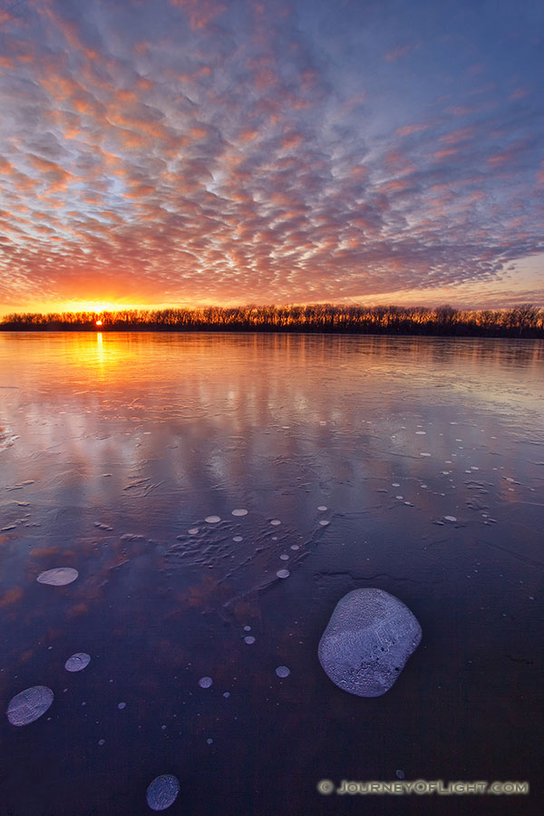 The warm setting sun shines brightly across the frozen lake on a chilly January evening before dipping below the horizon. - DeSoto Photography