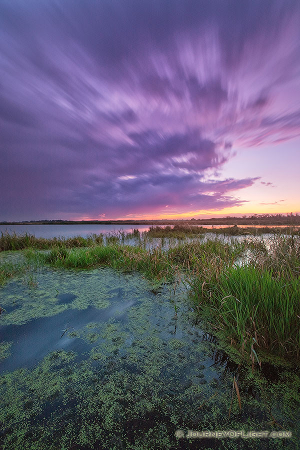 On a warm summer evening, the sun sets in the west as clouds roll over a salt creek marsh at Jack Sinn Wildlife Management Area. - Nebraska Photography