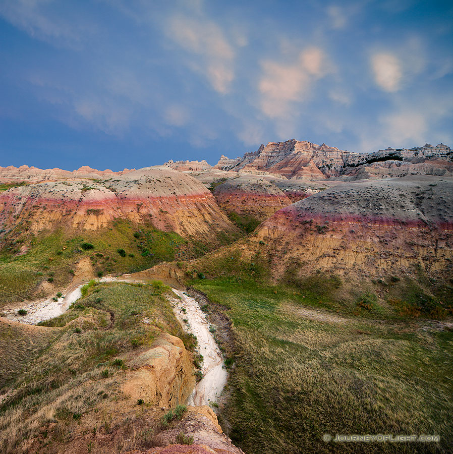 On a warm summer evening as I was photographing Badlands National Park in South Dakota, I could hear thunder in the distance.  As I continued to capture the landscape a patch of mammantus clouds began to creep closer.  Generally associated with severe thunderstorms, I began to get my gear ready in case things turned bad and I had to leave quickly.  Luckily, the wind shifted and the storm began to move away, just at the last light of day began to peak through the remaining clouds in the west illuminating the landscape. - South Dakota,Landscape Photography