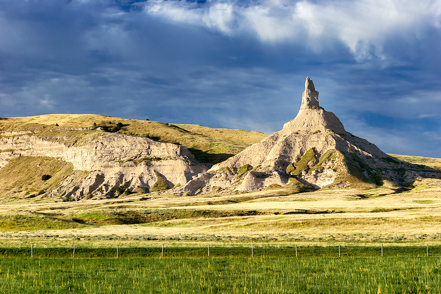 The spire known as Chimney Rock glows warm in the recent sunrise and the surrounding fields are a verdant green from a recent rain. - Nebraska Photography