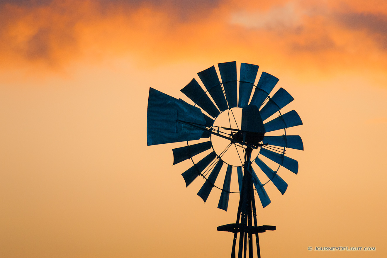 The orange glow of the sunset illuminates the last bits of clouds above an old windmill in western Iowa. - Iowa Picture