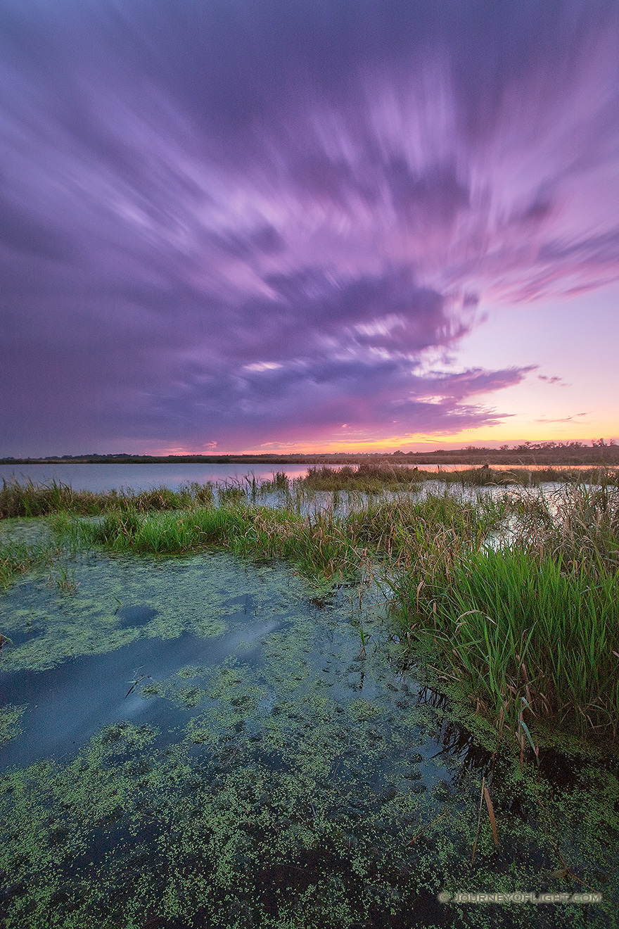 On a warm summer evening, the sun sets in the west as clouds roll over a salt creek marsh at Jack Sinn Wildlife Management Area. - Nebraska Picture