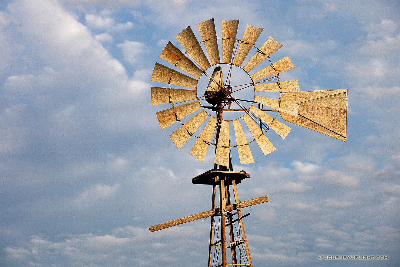In rural Dixon County in Northeastern Nebraska a still windmill reflects the golden light of the rising sun against a cloudy sky. - Nebraska Picture