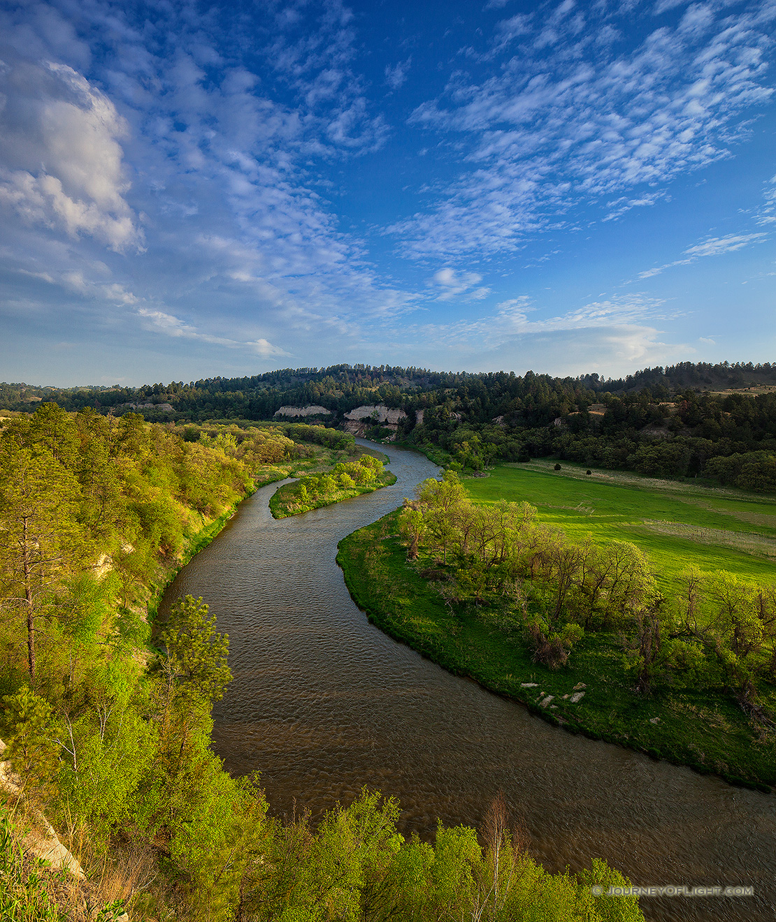 The Niobrara river, snakes through a lush green valley on a beautiful spring morning. A cool breeze blew gently as the sun rose in the east illuminating the clouds in the sky. - Valentine Picture