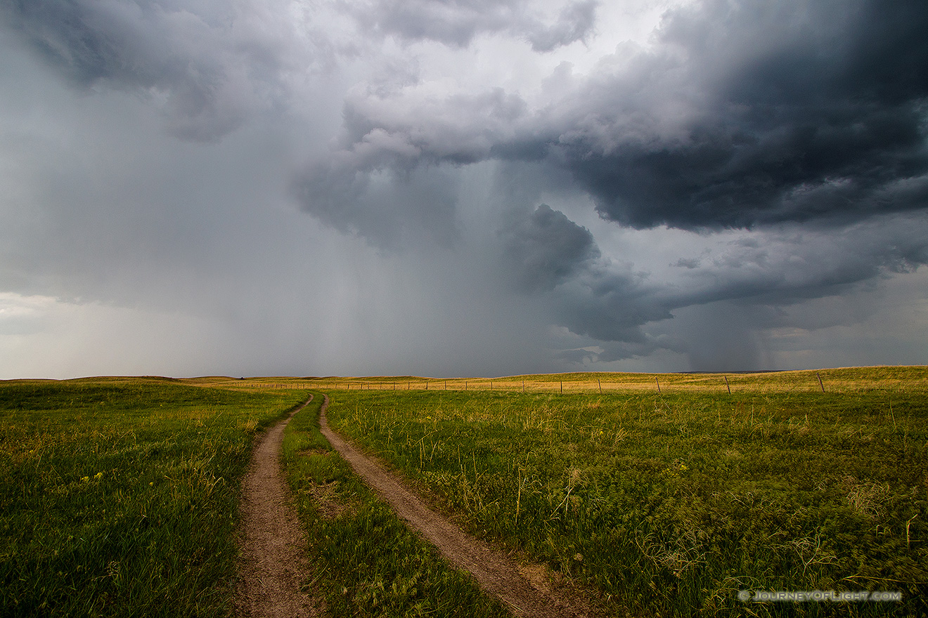 An ominous storm hovers over a two track in McKelvie National Forest.  The clouds slowly roll through dropping rain over the sandhills while lightning lights up the sky and the sound of thunder fills the air. - Sandhills Picture
