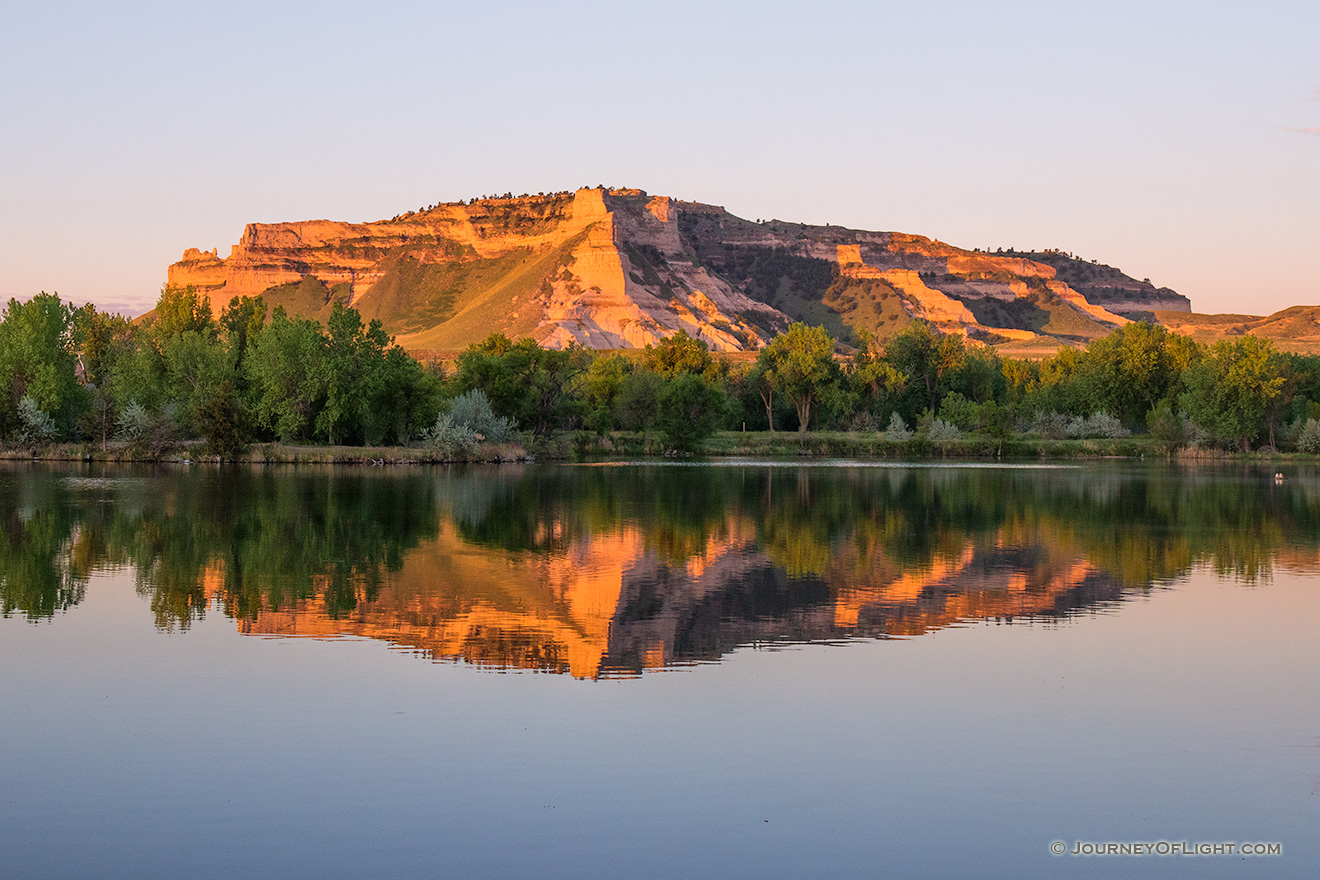 Glowing in the light of the recently risen sun, Scotts Bluff National Monument in western Nebraska is reflected in a small nearby lake. - Nebraska Picture