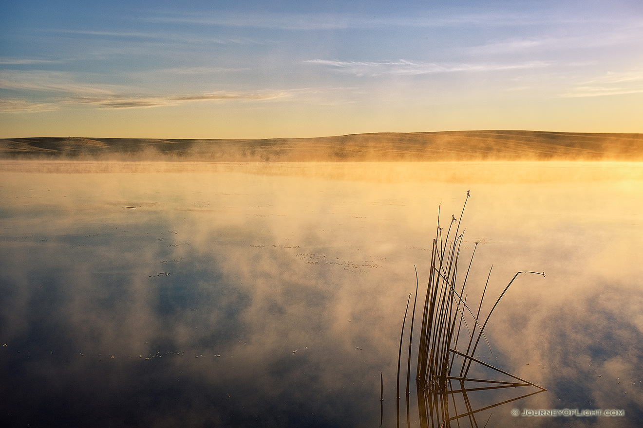 One of the most expansive and uninhabited areas of Nebraska also holds expansive beauty.  The Oglala National Grasslands in northwestern Nebraska represent some of the last native grasslands in the United States.  On a cool September morning a few years ago, I ventured out to the Meng Reservoir and captured the morning sun hitting the mist rising from the water.  The only sound was ducks quacking the distance welcoming the new day. - Nebraska Picture